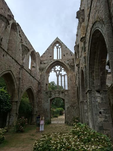 Two people stand inside a historic stone ruin surrounded by greenery.